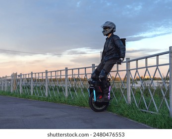 A man on an EUC monocycle in protective gear. Modern urban electric transport . A picturesque summer sunset