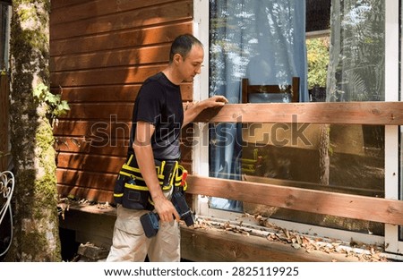 man on an extension ladder using a hammer to nail in new wood siding boards, homeowner maintenance and upkeep, making outdoor repairs on house 