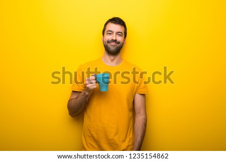 Man on isolated vibrant yellow color holding hot coffee in takeaway paper cup