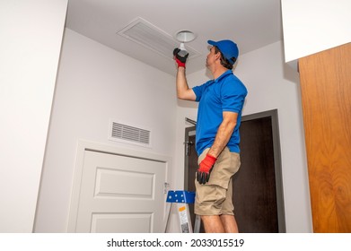 A Man On A Ladder Changing A Flood Light Bulb Inside Of A Home