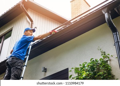 man on ladder cleaning house gutter from leaves and dirt