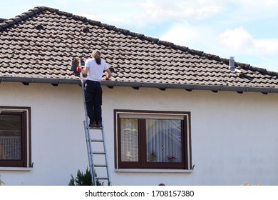 Man On Ladder Cleaning House Gutter From Leaves And Dirt