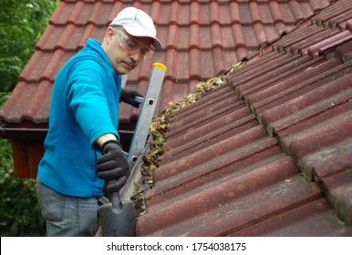 Man On Ladder Cleans Gutter On The Roof. Maintenance Of A Private Home.