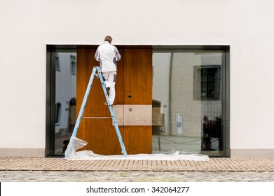 Man on a ladder painting an apartment block during exterior renovations.