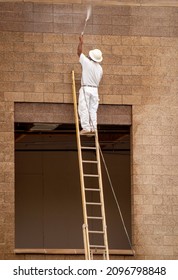 Man on a ladder power washing a wall dressed in white  - Shutterstock ID 2096798848