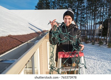 Man On A Ladder Putting Up Exterior Christmas Lights On His House And Trying To Untangle The Lights 