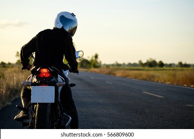 A Man On The Motorcycle Parking On The Road Left Side And Sunset, To Looking Behind.