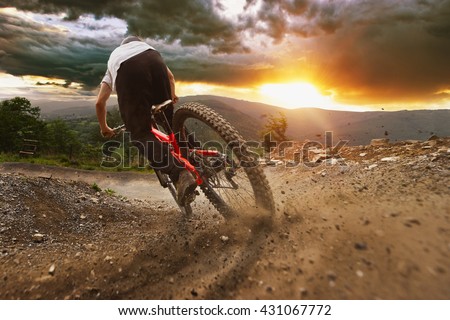 Man on mountain bike rides on the trail on a stormy sunset.