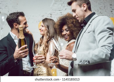 Man, on new year or birthday party opening bottle of champagne together with his friends