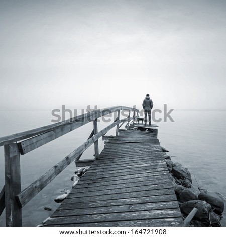 A man on the old broken wooden pier starring at the foggy Sea
