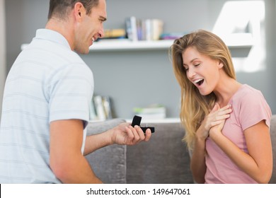 Man On One Knee Proposing To Surprised Girlfriend In Sitting Room At Home