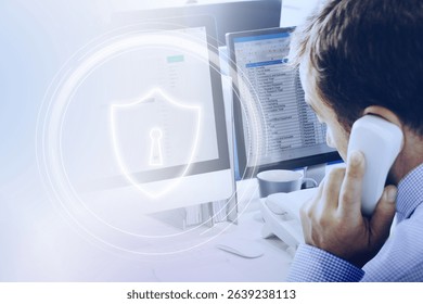 Man on phone at desk, computer screen with security shield icon. Office setting, focus on cybersecurity. Professional environment, cybersecurity theme, data protection. Professional business people. - Powered by Shutterstock - Get 15% off with code: PIKWIZARD15