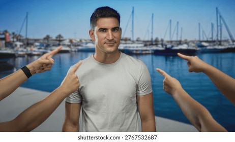 Man on a port dock with multiple hands pointing fingers at him, pointing gesture and bare forearms visible; shame judgment.