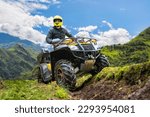 Man on quad bike. Guy on ATV in mountains. Off-road driving. Quad biker loves extreme sports. Male ATV driver. Extreme man looks away. Dangerous sports with ATV. Quad bike driver under blue sky