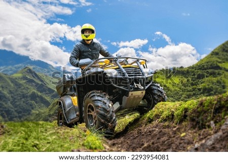 Man on quad bike. Guy on ATV in mountains. Off-road driving. Quad biker loves extreme sports. Male ATV driver. Extreme man looks away. Dangerous sports with ATV. Quad bike driver under blue sky