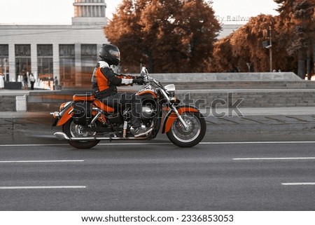 A man on a red cruiser motorcycle rides through the city in autumn. A motorcyclist travels on a motorbike, a lifestyle. Biker riding on the city roads.