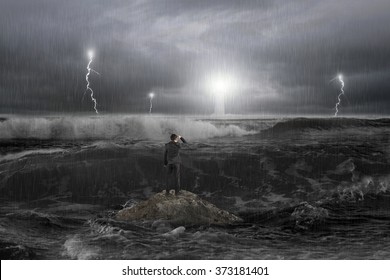 Man on rock gazing at lighthouse in the ocean with storm, thunder, lightening and waves in dark  - Powered by Shutterstock