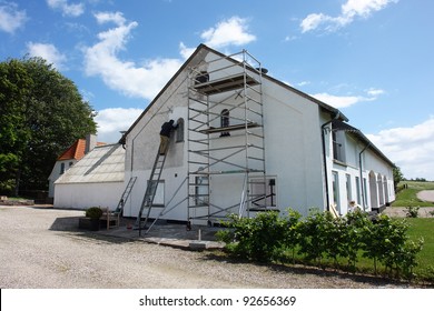 Man On Scaffolds Painting A House During Exterior Renovations