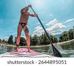 Man on a stand up paddle board in the lake of Levico in Trentino, Northern Italy. The man is forty years old and is a caucasian with light eyes and hair