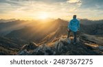 Man on stone on the hill and beautiful mountain valley in haze at colorful sunset in autumn. Dolomites, Italy. Guy, mountain ridges in fog, orange grass and trees, blue sky with sun in fall. Hiking	