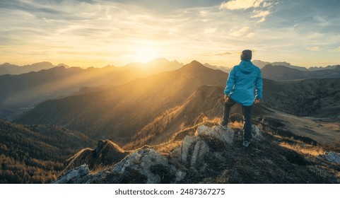 Man on stone on the hill and beautiful mountain valley in haze at colorful sunset in autumn. Dolomites, Italy. Guy, mountain ridges in fog, orange grass and trees, blue sky with sun in fall. Hiking	 - Powered by Shutterstock