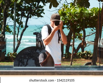 A man on the street photographs himself in the reflection of the building. On the ocean. Sunny day. Dominican Republic.