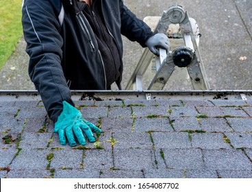 Man On Top Of Ladder Cleaning Moss And Dirt From A Building Roof - His Hand In Messy Gloves - View From The Top Of The Roof