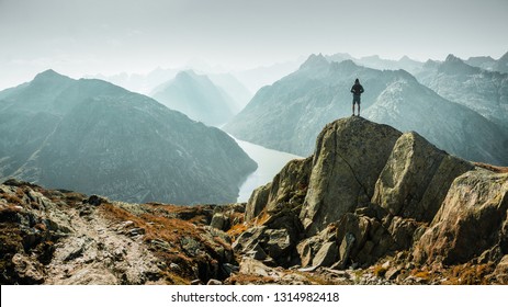 
Man On Top Of Mountain. Epic Shot Of Adventure Hiking In Mountains Alone Outdoor Active Lifestyle Travel Vacations. Conceptual Scene. 