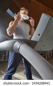 Man On A Treadmill Putting On A Ffp2 Face Mask During Pandemic Coronavirus.