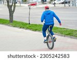 Man on unicycle moving along sidewalk. Elderly person ride on one wheel bike. Man riding monocycle at city street, active lifestyle
