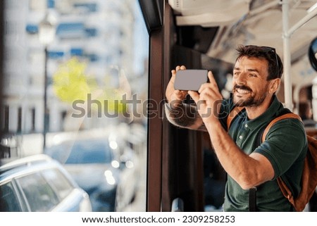 A man on vacation is riding a public bus and taking photos trough the window.