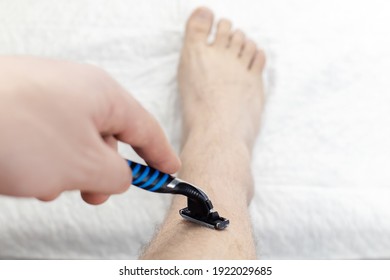 A Man On A White Background Shaves His Legs. Hairy Legs And Care For Them. Gender Equality Concept. A Close-up Showing The Foam, Razor, And Shaved Hair On A Smooth Leg.