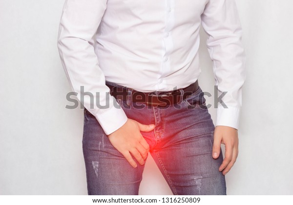 A man on a white background in a white\
shirt holding on to his groin he has pain and varicocele of the\
spermatic cord, a problem, varicose\
veins