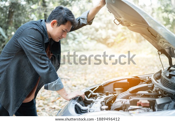 Man open\
car hood for repair as maintenance service. Man trying to repair a\
car engine, looking inside open\
bonnet