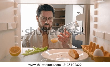 Man open empty refrigerator with half lemon lettuce leaf one egg slice of bread leftover orange juice in bottle find solution order food delivery with mobile phone app point of view from inside fridge