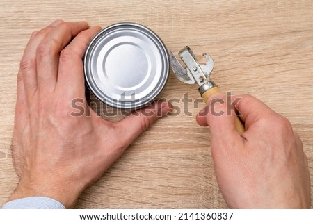Man opening a can with a can opener. Canned food.