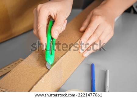 Man opening cardboard box with utility knife on grey background, closeup