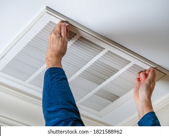 Man opening ceiling air vent to replace dirty HVAC air filter. Home air duct system maintenance for clean air. - Shutterstock ID 1821588962