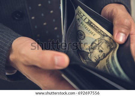 A man opening wallet showing some money, 20 US dollar bill left