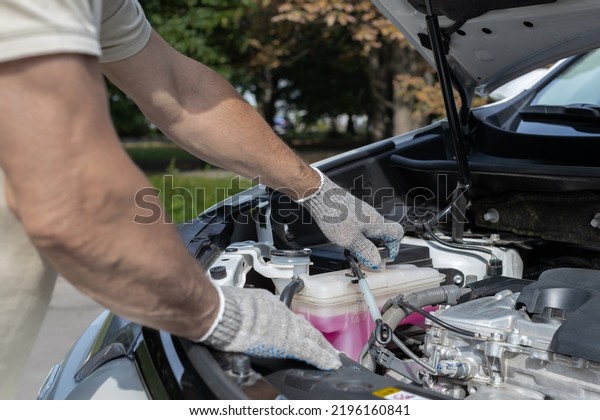 man opens cap of expansion tank in car.\
hand opens cap of car coolant expansion\
tank