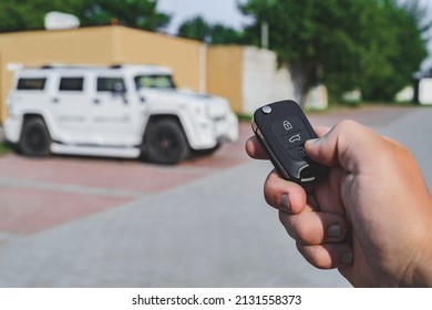 A man opens the car with a key fob, In the background is a white SUV car