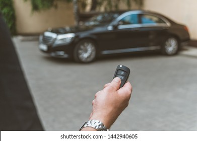 The man opens the car with a keychain, in the background is a black car