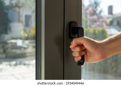 Man opens or closes the metal or PVC door. Hand holding aluminum window handle closeup view. Energy efficient, security profile, blur garden outdoor background