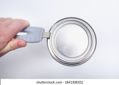 A Man Opens A Jar Of White Paint With A Can Opener On A White Background. Renovation Concept.