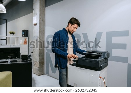 Man operates a printer in a modern office environment during daylight, focused on completing tasks efficiently and professionally