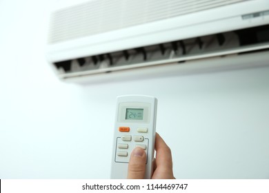Man operating air conditioner with remote control indoors - Shutterstock ID 1144469747