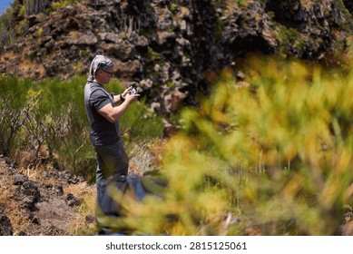 Man operating a drone controller among endemic scrub on a volcanic hillside near Masca in the Teno massif