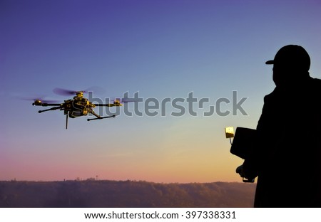 Man operating a drone with remote control. Dark silhouette against colorful sunset. Soft focus.