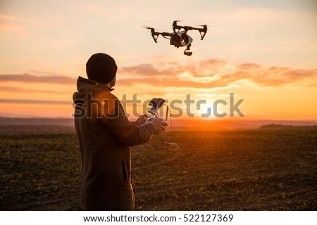Man operating a drone with remote control. Dark silhouette against colorful sunset. Soft focus.