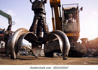 Man operating excavator industrial machine with mechanical grabber used for lifting scrap metal in junk yard. - Powered by Shutterstock